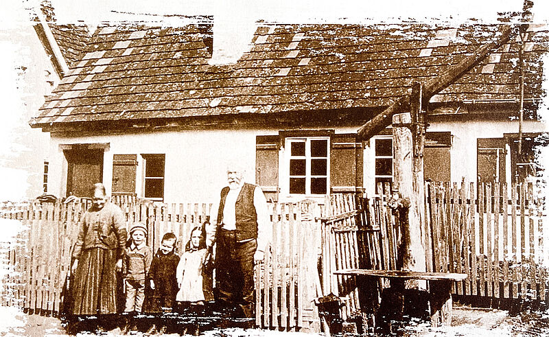 Familie steht vor einem Haus, daneben ein großer Brunnen Familie steht vor einem Haus, daneben ein großer Brunnen