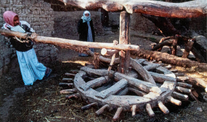 Eine großes Holzrad wird von einer Frau über einen Ast angetrieben Eine großes Holzrad wird von einer Frau über einen Ast angetrieben