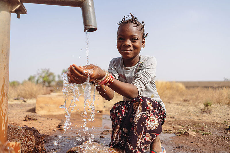 Mädchen kniet an einem Brunnen und hält die Hände auf, im Hintergrund Afrikanische Steppe. Mädchen kniet an einem Brunnen und hält die Hände auf, im Hintergrund Afrikanische Steppe.