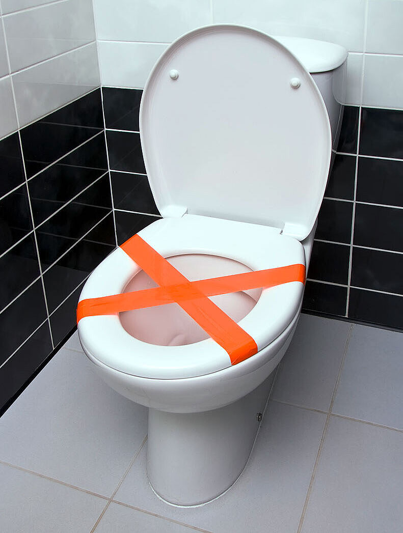 Eine aufgeklappte Toilette, die mit rotem Band abgeklebt ist, damit niemand etwas hineinwerfen kann. Eine aufgeklappte Toilette, die mit rotem Band abgeklebt ist, damit niemand etwas hineinwerfen kann.