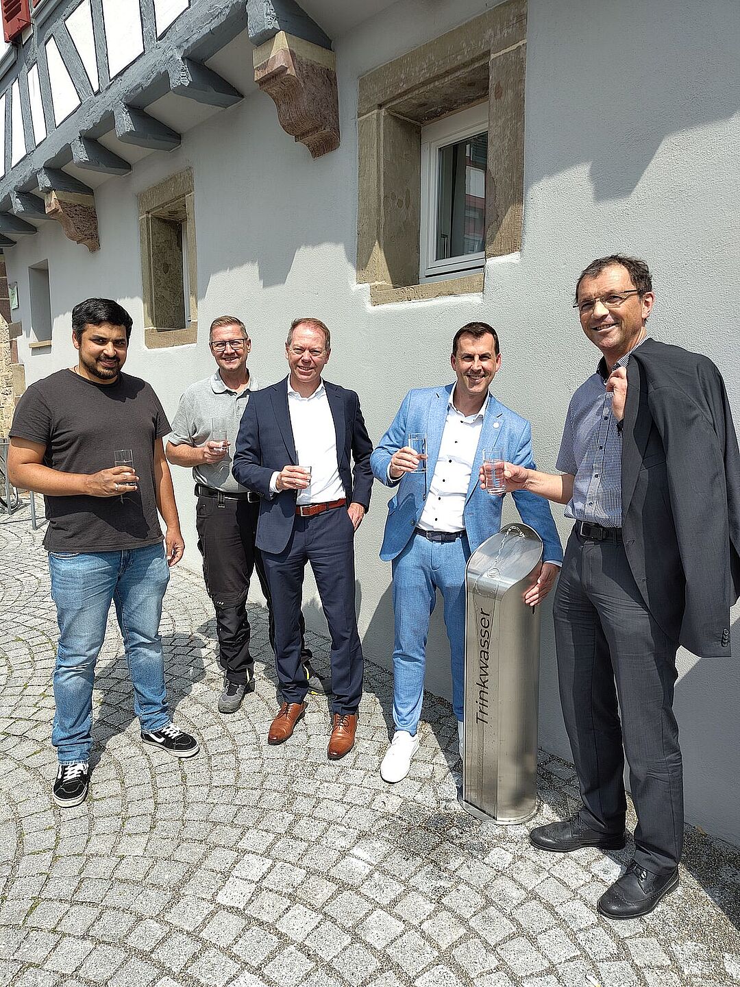 2025_08_06_Winterbach_Einweihung_Trinkwasserbrunnen Fünf Männer vor einem Trinkwasserbrunnen vor dem Rathaus