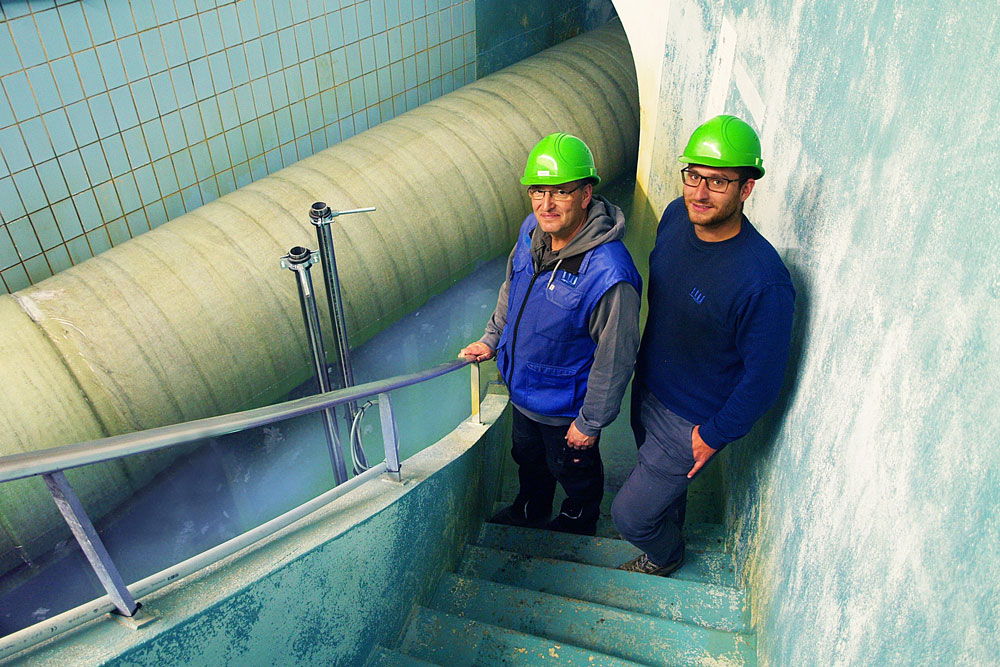 Zwei Junge Männer mit Schutzhelm stehen auf einer Treppe, unter ihnen verläuft ein Rohr Zwei Junge Männer mit Schutzhelm stehen auf einer Treppe, unter ihnen verläuft ein Rohr