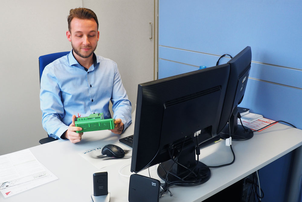 Mann sitzt am Schreibtisch und hält ein elektronisches Gerät in den Händen Mann sitzt am Schreibtisch und hält ein elektronisches Gerät in den Händen
