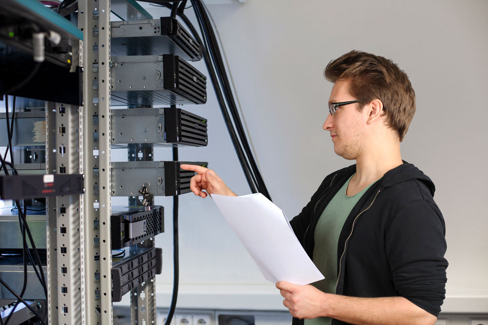 Junger Mann kontrolliert etwas am Serverschrank Junger Mann kontrolliert etwas am Serverschrank