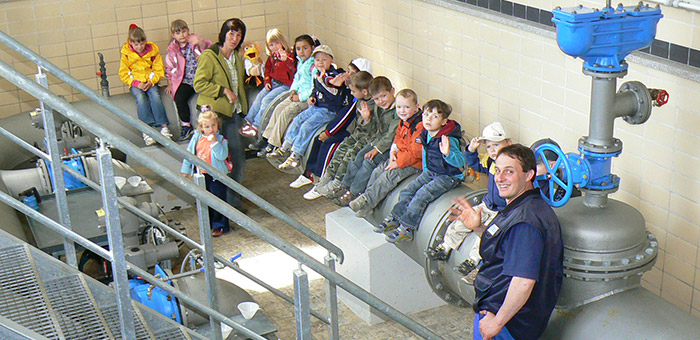 Eine Gruppe Kindergartenkinder sitzt auf einer großen Wasserleitung