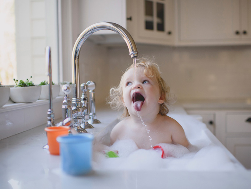 Kind badet und trinkt Wasser aus Hahn