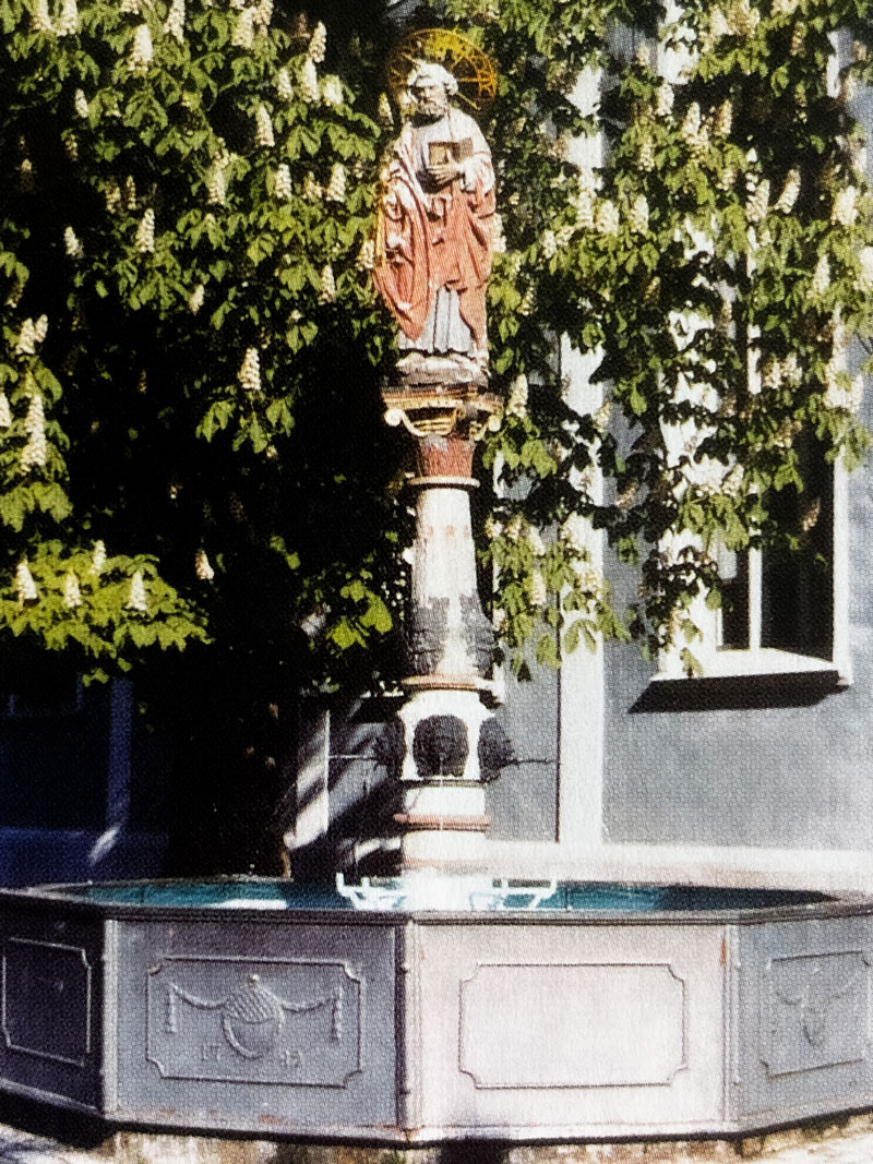 Ein Brunnen unter einem Baum, im Hintergrund ein Haus Ein Brunnen unter einem Baum, im Hintergrund ein Haus