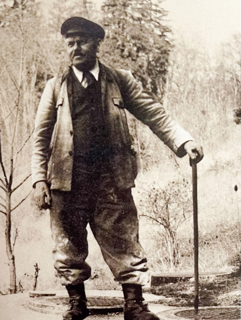Mann, gekleidet in Uniform und Kappe stützt sich auf einen Stock und steht in Landschaft, am Boden Behälterdeckel. Mann, gekleidet in Uniform und Kappe stützt sich auf einen Stock und steht in Landschaft, am Boden Behälterdeckel.